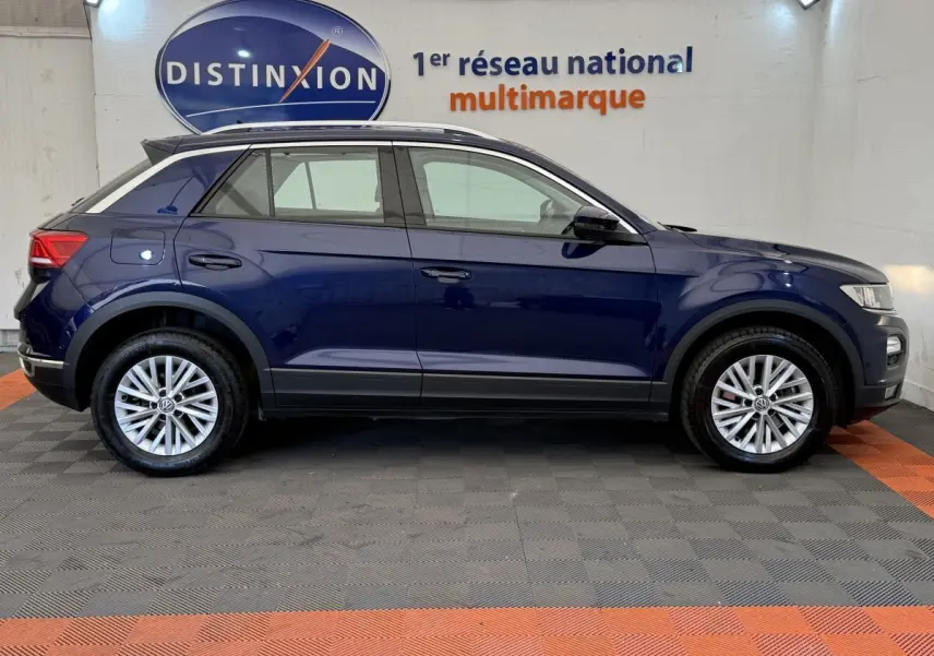 Vue de profil côté gauche d'un Volkswagen T-Roc bleu 2020 stationné en intérieur avec jantes argentées et toit noir.