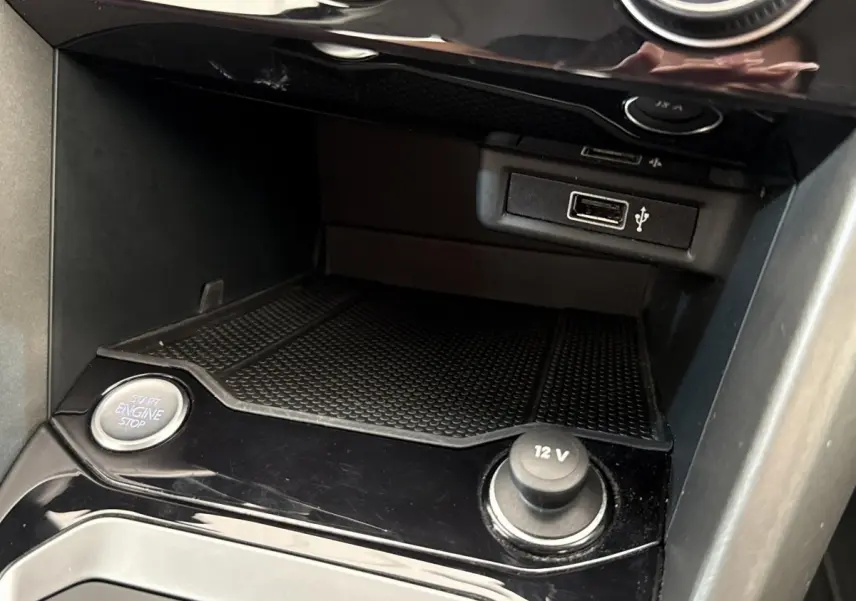Gros plan intérieur sur la console centrale du Volkswagen T-Roc bleu, montrant bouton start/stop et prise 12V.