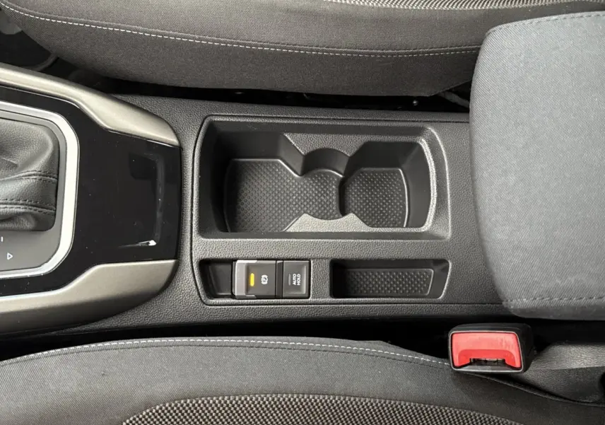 Vue plongeante sur la console centrale noire du Volkswagen T-Roc bleu, avec porte-gobelets et frein à main électrique.