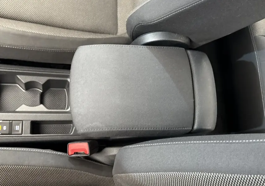 Vue rapprochée de l'accoudoir central et console noire du Volkswagen T-Roc bleu, avec bouton de frein à main électrique visible.