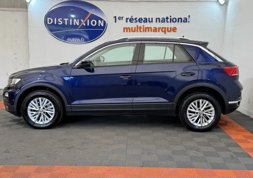 Vue latérale droite d'un Volkswagen T-Roc bleu 2020, avec jantes alliage et barres de toit noires visibles.