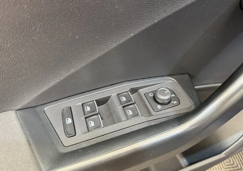 Gros plan sur les commandes électriques des vitres et rétroviseurs sur la porte avant gauche d’un Volkswagen T-Roc bleu.