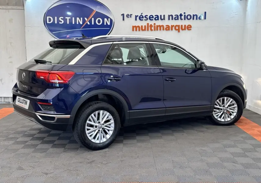 Volkswagen T-Roc bleu en vue profil droit, avec toit noir et jantes alliage, stationné en intérieur showroom.