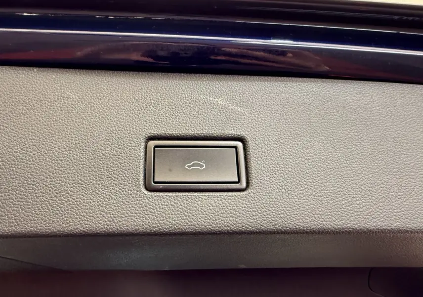 Bouton d'ouverture électrique du coffre sur la garniture intérieure grise d'un Volkswagen T-Roc bleu.