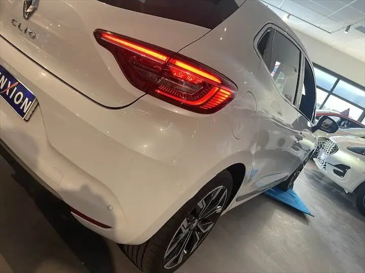 Vue 3/4 arrière droite d'une Renault Clio V blanc nacré avec feux LED allumés dans un showroom.
