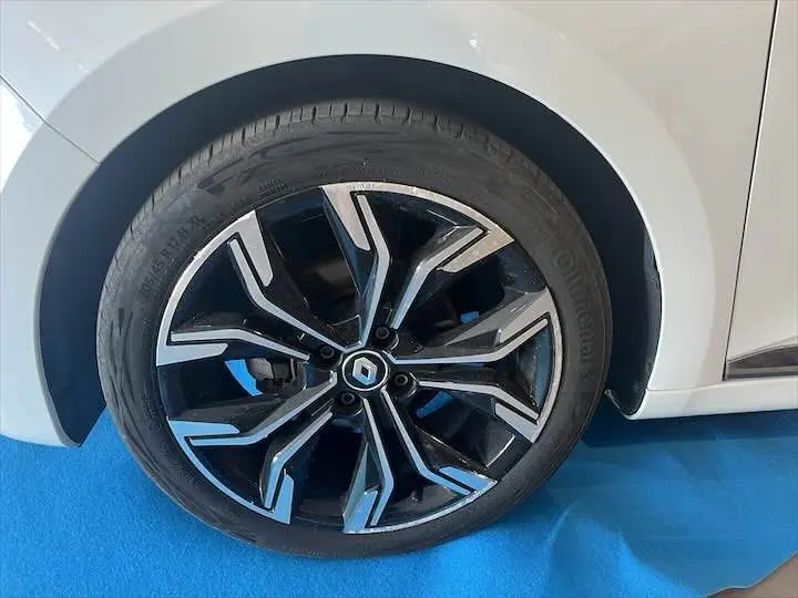 Gros plan sur la roue avant droite de la Renault Clio V blanche nacrée, avec jante alliage noire et argentée au design moderne.