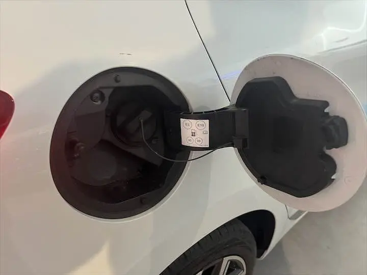 Ouverture de la trappe à carburant côté gauche d'une Renault Clio V blanc nacré, montrant le bouchon essence et l'intérieur de la trappe.