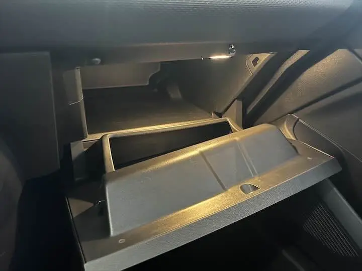 Gant de boîte à gants ouvert côté passager dans l'habitacle sombre d'une Renault Clio V blanche nacrée.