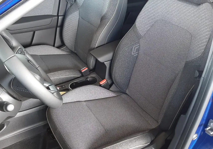 Intérieur du Renault Captur E-Tech Hybrid 2024 vu côté conducteur, sièges gris foncé avec surpiqûres claires, portière bleu iron ouverte.