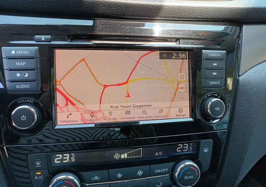 Tableau de bord du Nissan Qashqai blanc nacré 2019 montrant l'écran GPS avec carte et commandes climatisation digitales.