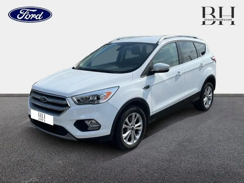 Ford Kuga blanc glacier vu en 3/4 avant droit, avec barres de toit aluminium et jantes alliage.