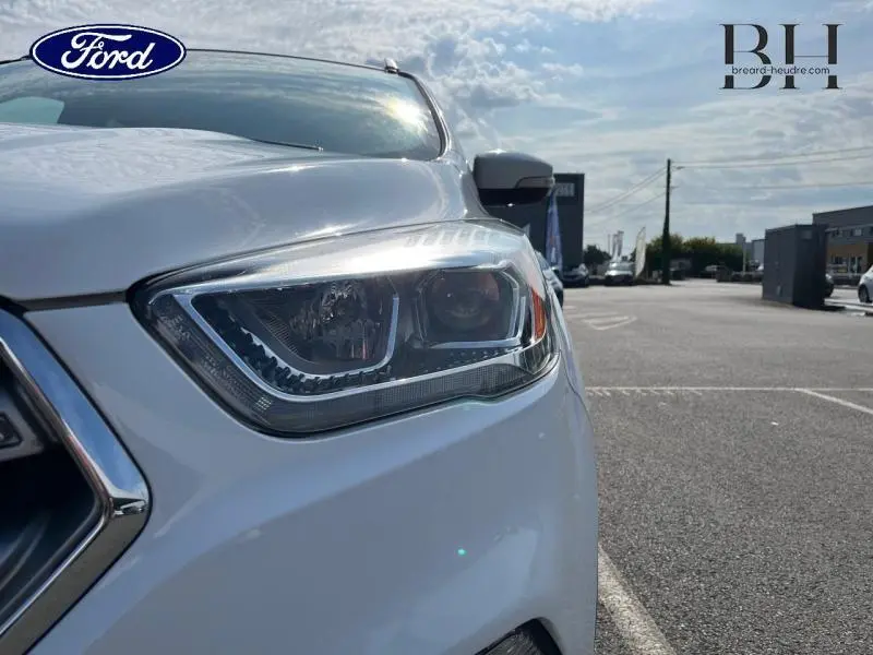 Gros plan sur le phare avant droit du Ford Kuga blanc glacier, soulignant ses lignes modernes et son chrome brillant.