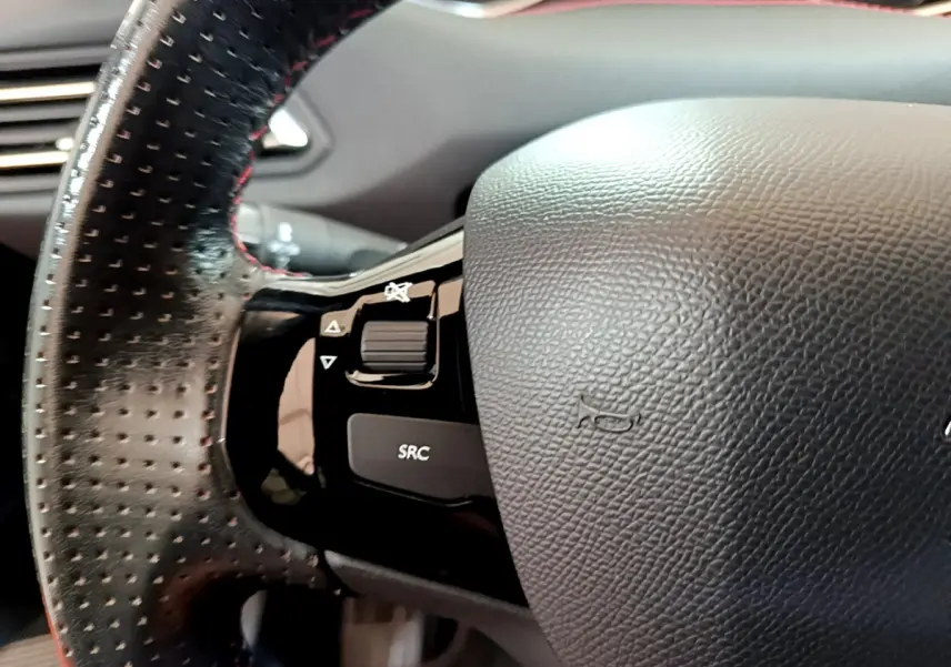 Gros plan sur le volant cuir perforé côté gauche du Peugeot 308 gris foncé, avec commandes audio intégrées.