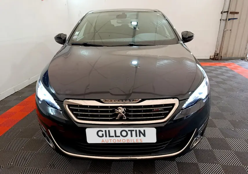 Vue frontale d'une Peugeot 308 gris foncé avec phares LED allumés dans un showroom intérieur.