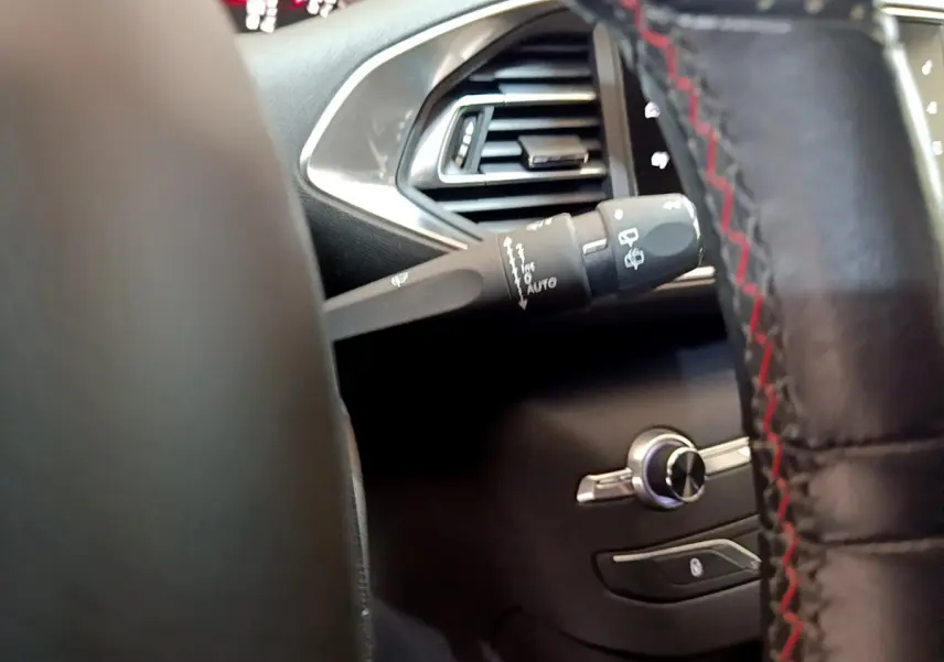 Gros plan sur la commande d'essuie-glace à gauche du volant cuir avec surpiqûres rouges dans l'habitacle gris foncé Peugeot 308.