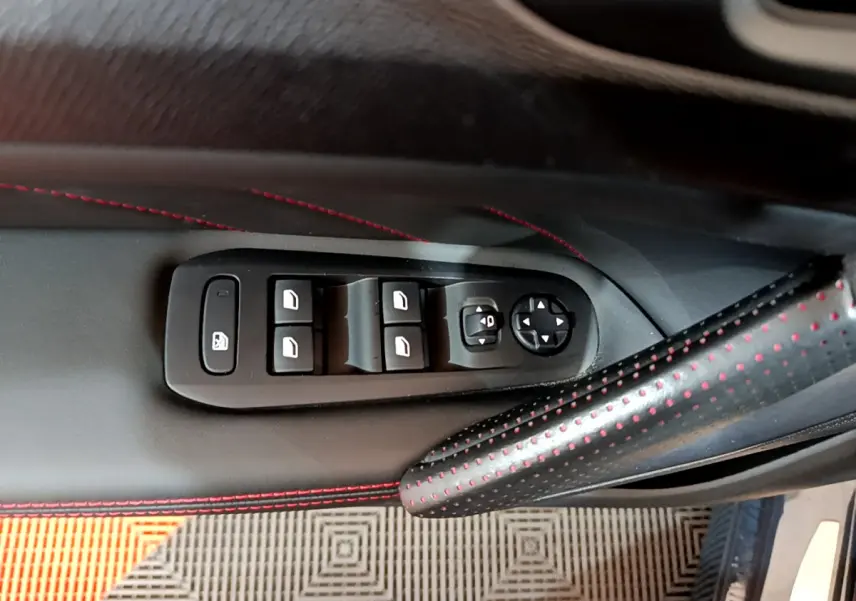 Gros plan sur la commande des vitres et rétroviseurs côté conducteur du Peugeot 308 gris foncé avec surpiqûres rouges.