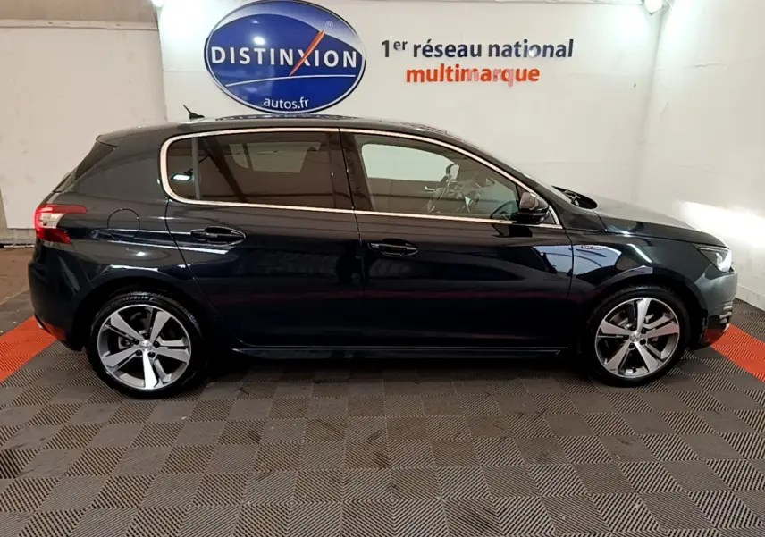 Profil côté gauche d'une Peugeot 308 gris foncé 2016 GT Line avec jantes alliage et vitres teintées en intérieur showroom.