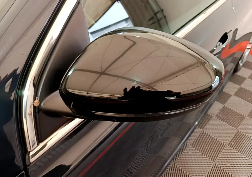 Rétroviseur côté gauche noir brillant du Peugeot 308 gris foncé, avec reflet de l'environnement intérieur.