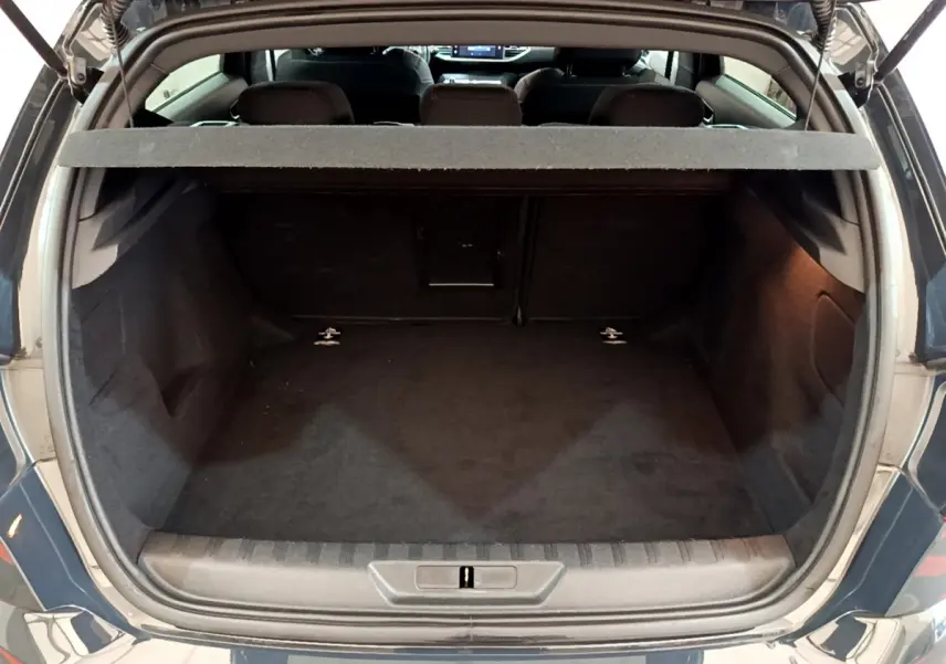 Coffre ouvert vu de l'arrière d'une Peugeot 308 gris foncé, montrant l'espace de chargement vide et la tablette de séparation.