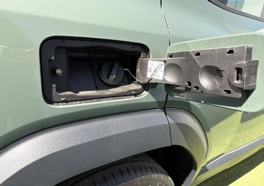 Détail de la trappe à carburant ouverte côté gauche du Dacia Duster III kaki lichen, avec partie arrière du véhicule visible.