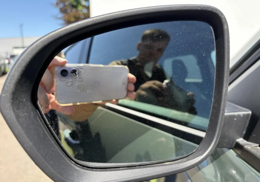 Rétroviseur extérieur côté gauche du Dacia Duster kaki lichen, avec reflet partiel du véhicule et d'une personne.