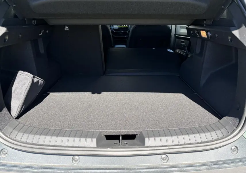 Vue du coffre ouvert du Dacia Duster III 1.8 Hybrid 155, montrant la banquette arrière rabattue et le tapis de coffre gris.