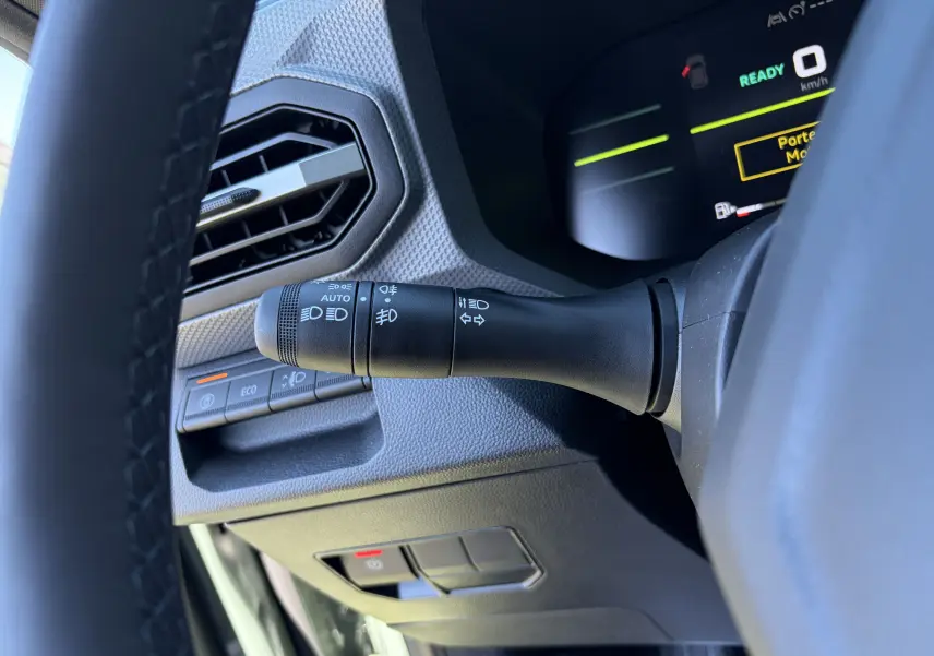 Gros plan côté gauche du volant du Dacia Duster III kaki, montrant la commande des phares et l'aération hexagonale.