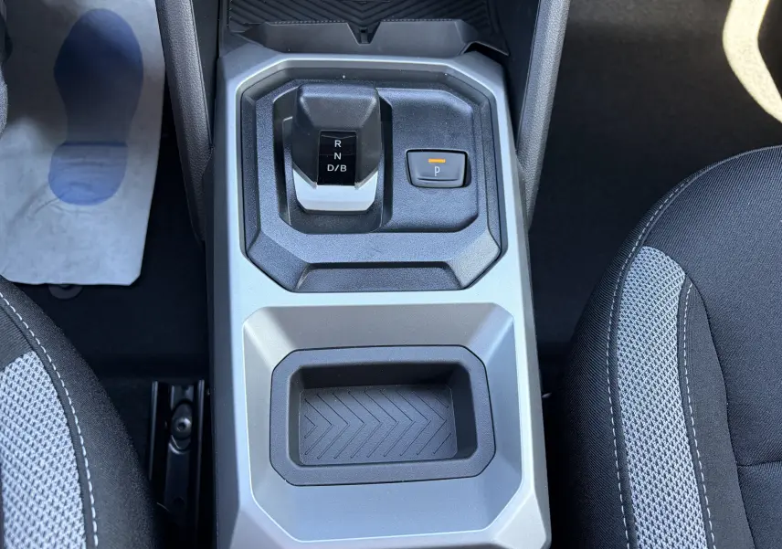 Vue plongeante sur la console centrale du Dacia Duster III hybride, avec levier de boîte auto et bouton de frein à main électrique.