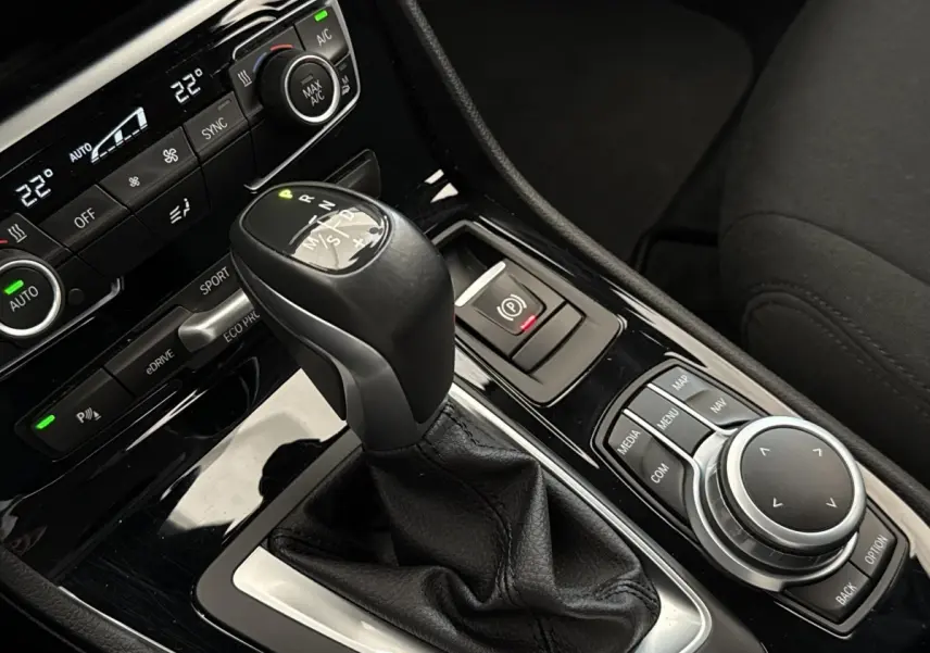 Gros plan sur la console centrale noire avec levier de vitesses et commandes multimédia d'une BMW Série 2 Active Tourer gris foncé.