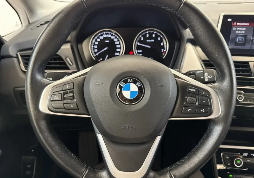 Vue rapprochée du volant cuir noir de la BMW Série 2 Active Tourer 225xe avec tableau de bord et écran tactile visibles.
