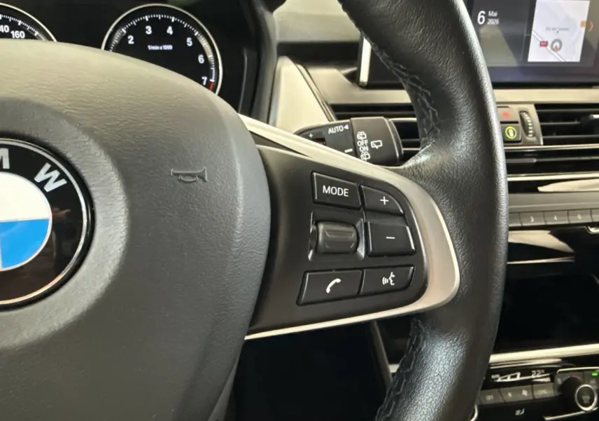 Gros plan sur le volant cuir noir de la BMW Série 2 Active Tourer 225xe, avec commandes multifonctions visibles et tableau de bord en arrière-plan.