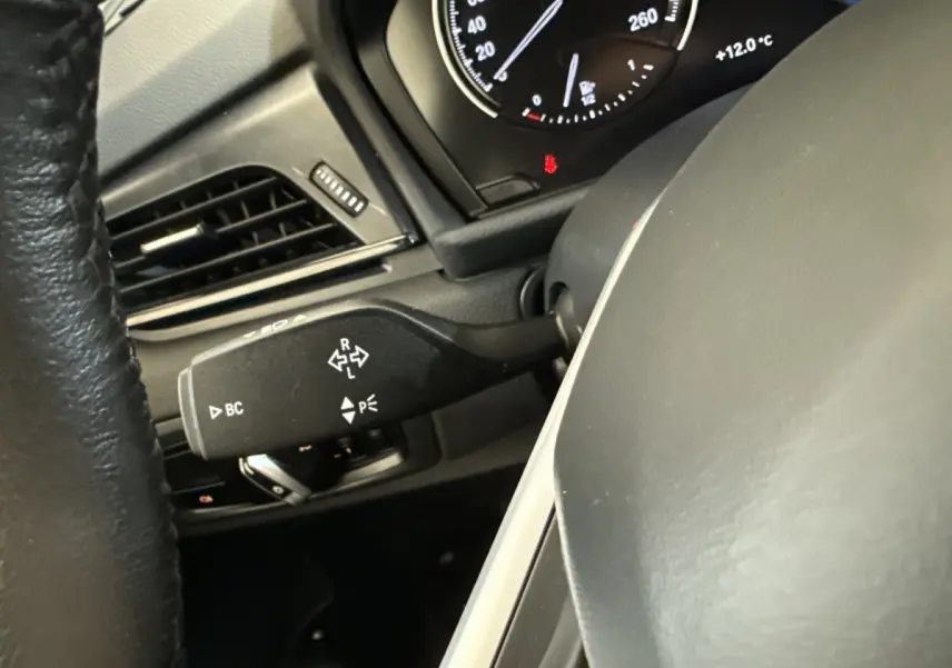 Gros plan sur le commodo de clignotant noir à gauche du volant dans l’habitacle d’une BMW Série 2 Active Tourer gris foncé.