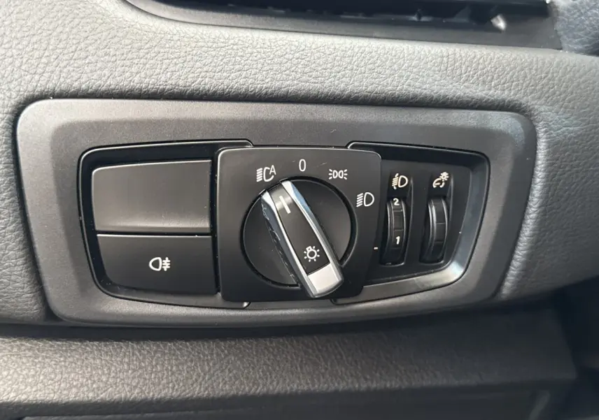 Gros plan sur le bouton de commande des phares et réglages lumineux dans l’habitacle d’une BMW Série 2 Active Tourer gris foncé.