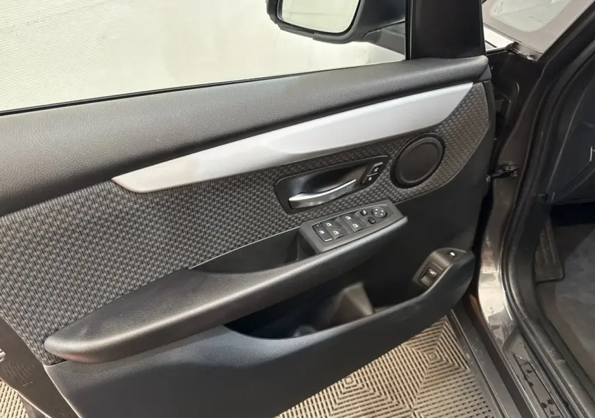 Vue intérieure côté gauche de la porte avant gris foncé d’une BMW Série 2 Active Tourer avec garniture carbone et commandes électriques.
