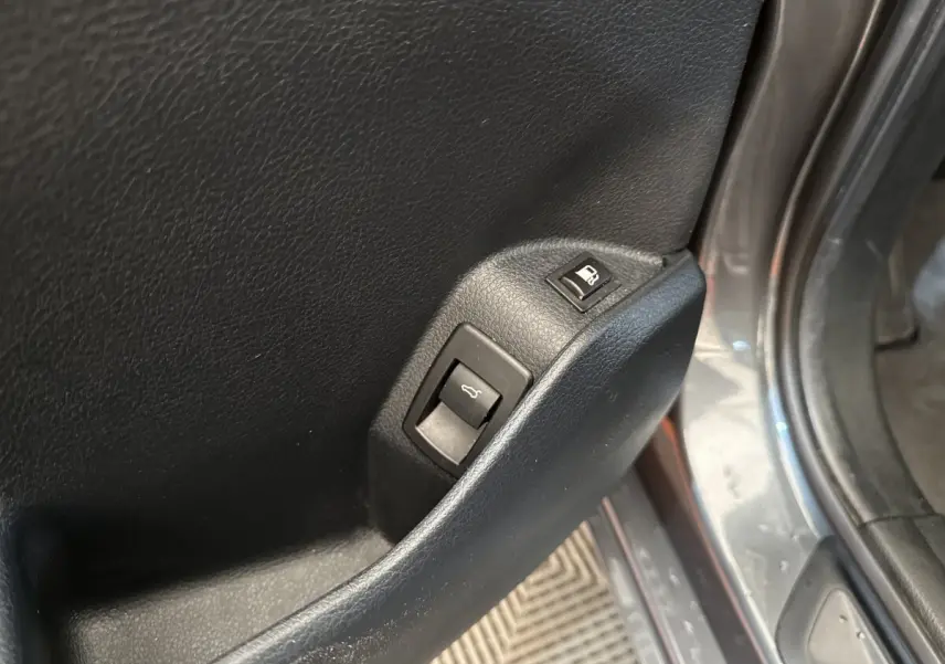 Gros plan sur les commandes d'ouverture du coffre et de la trappe à carburant sur la porte côté conducteur d'une BMW Série 2 Active Tourer gris foncé.