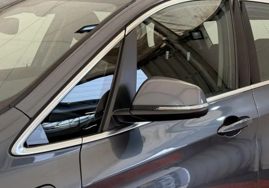 Gros plan sur le côté gauche gris foncé d'une BMW Série 2 Active Tourer avec rétroviseur et poignée de porte visibles.