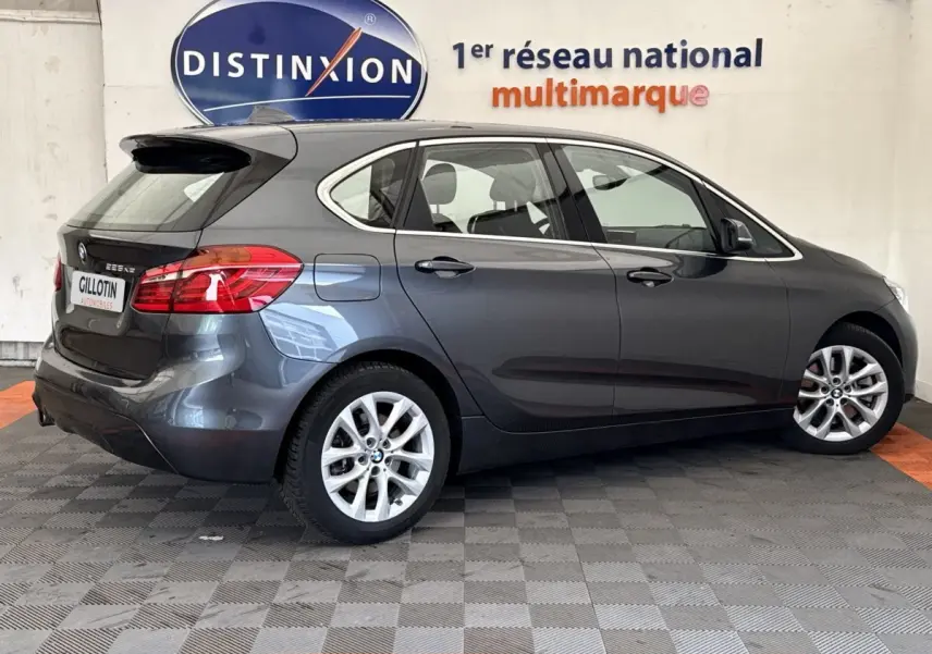 BMW Série 2 Active Tourer 225xe gris foncé vue de profil droit en intérieur avec logo Distinxion en arrière-plan.