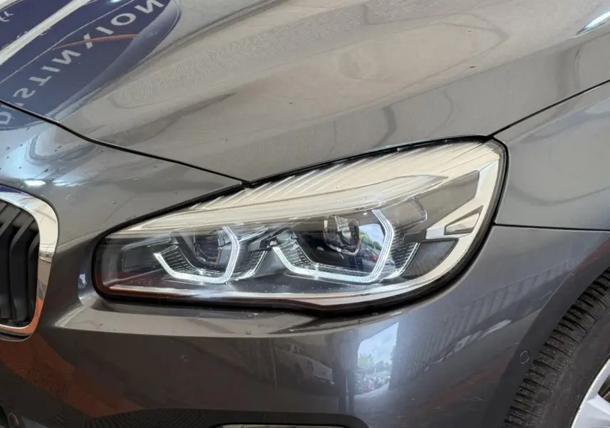 Gros plan sur le phare avant droit d'une BMW Série 2 Active Tourer gris foncé avec détails LED distinctifs.