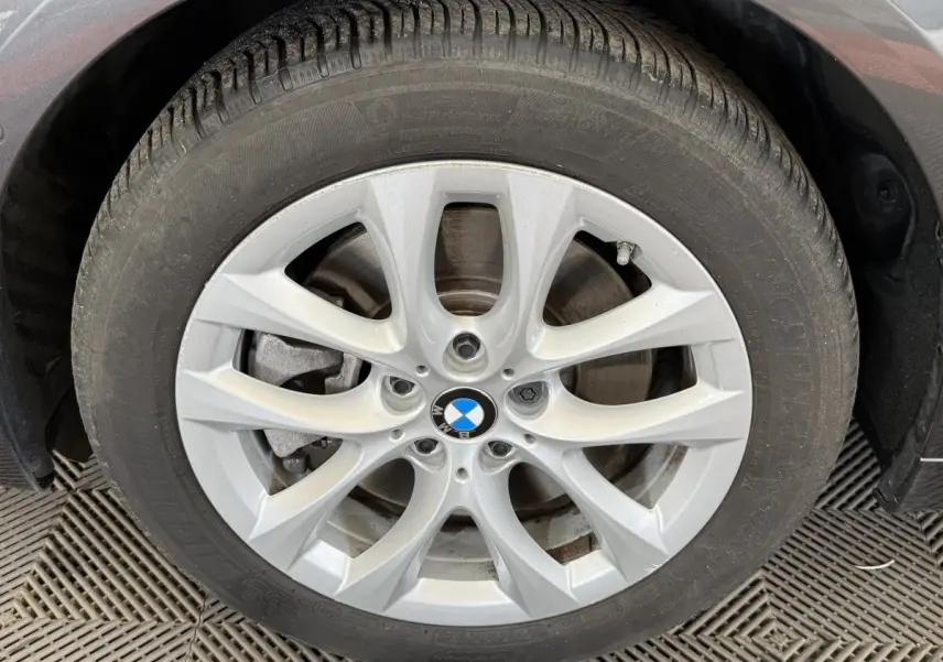 Gros plan sur la roue avant gauche avec jante argentée et logo BMW sur véhicule gris foncé.