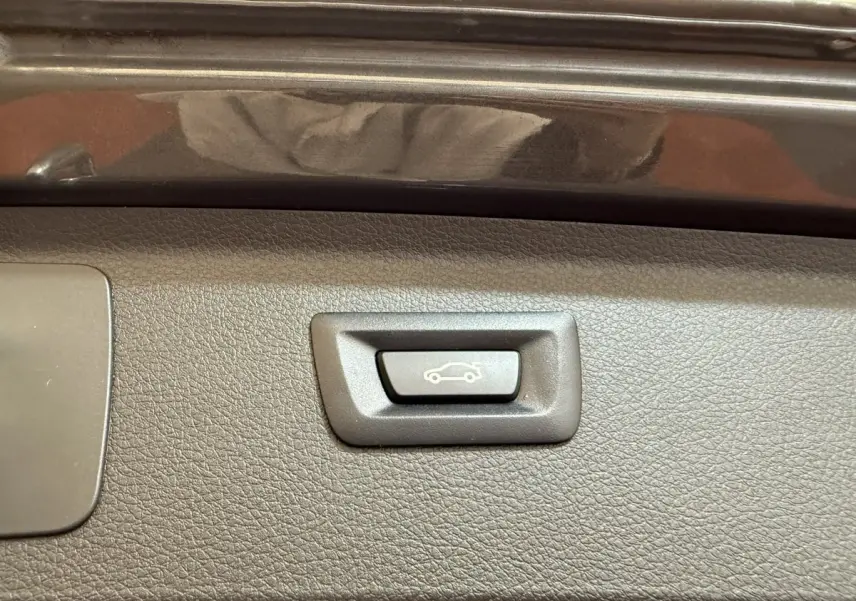 Gros plan sur le bouton d'ouverture électrique du coffre, intérieur noir texturé de la BMW Série 2 Active Tourer gris foncé.