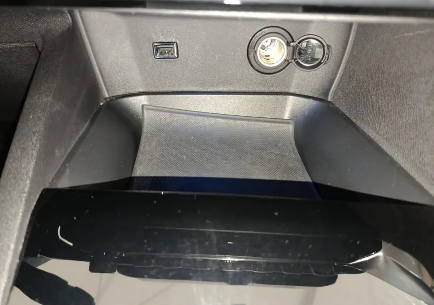 Gros plan sur la console centrale noire du Peugeot 3008 bleu, avec prise USB et allume-cigare visibles.