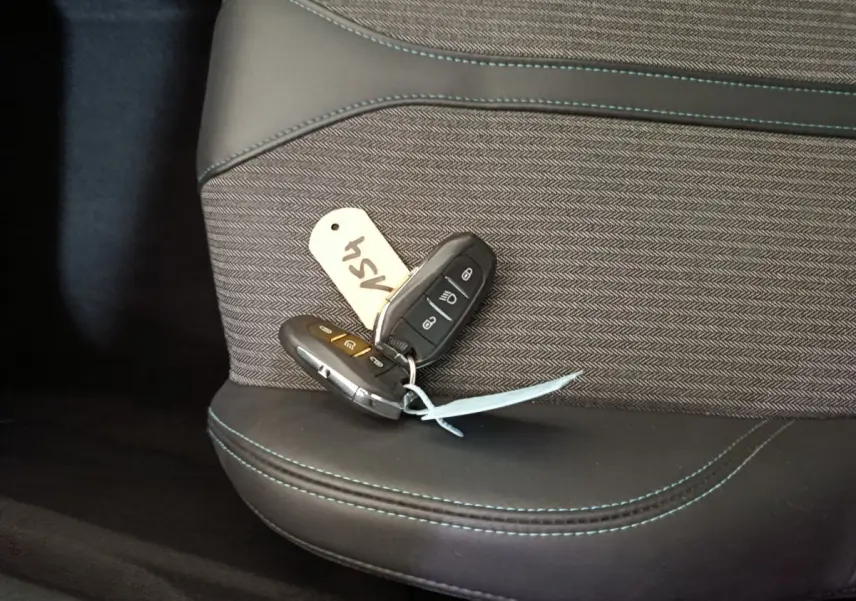 Gros plan sur les clés posées sur la sellerie noire et grise avec surpiqûres bleues du siège avant d'un Peugeot 3008 bleu.