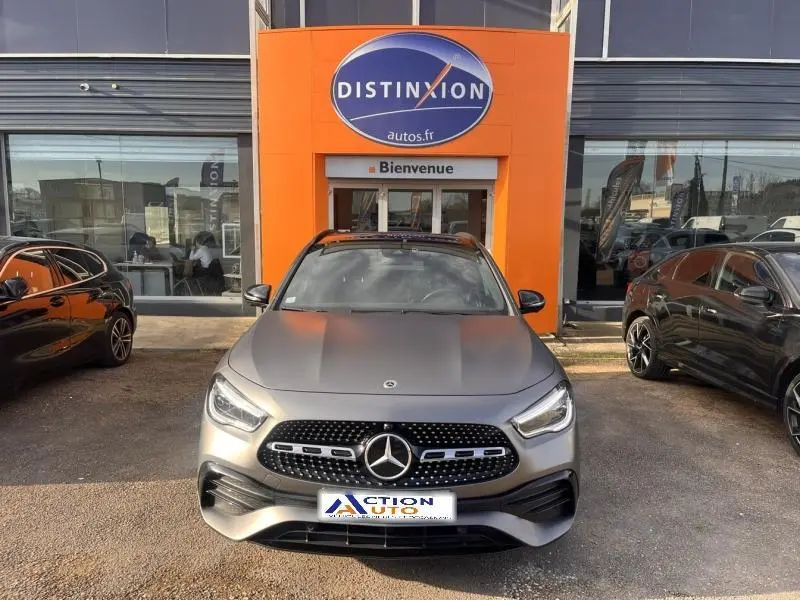 Vue de face d'une Mercedes GLA 200 d AMG Line gris montagne mat, calandre noire à étoiles chromées, stationnée devant un concessionnaire.