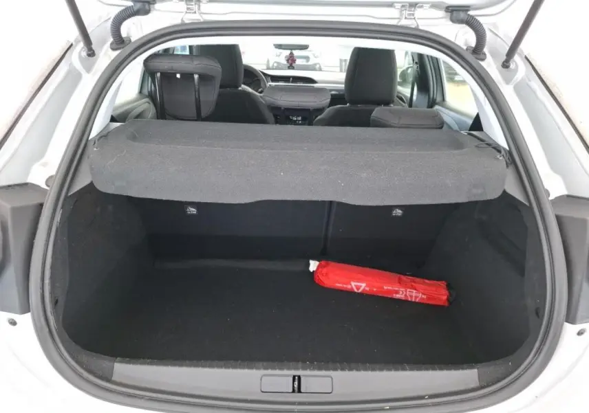 Vue arrière du coffre ouvert d'une Opel Corsa gris clair, avec cache-bagages et un triangle de sécurité rouge à l'intérieur.