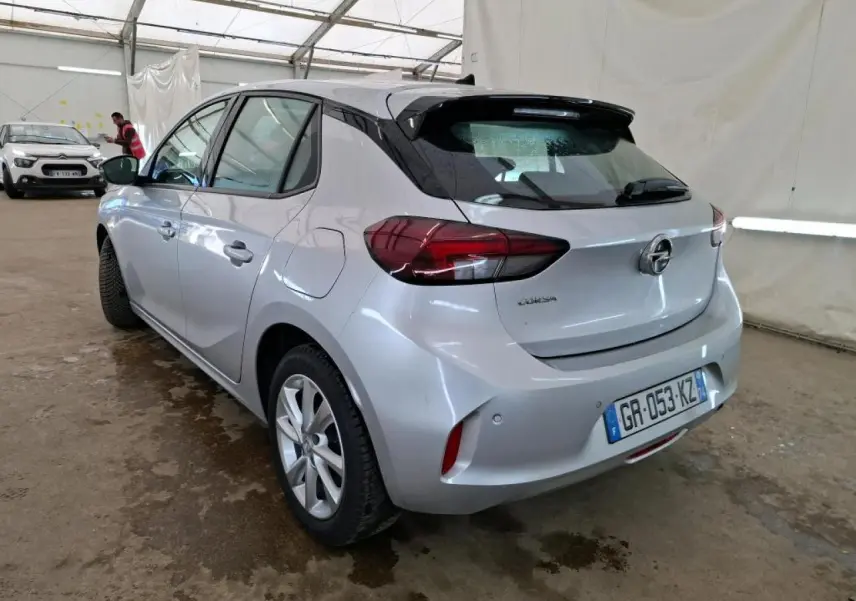 Vue 3/4 arrière gauche d'une Opel Corsa gris clair avec jantes alliage 16'' et rétroviseurs noirs dans un garage.