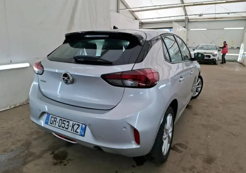 Vue 3/4 arrière droite d'une Opel Corsa gris clair avec jantes alliage 16'' dans un garage fermé.