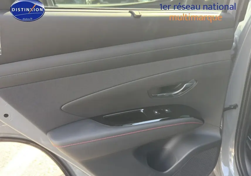 Vue intérieure de la porte arrière droite gris shadow du Hyundai Tucson 2026 avec surpiqûres rouges et commandes de vitres.