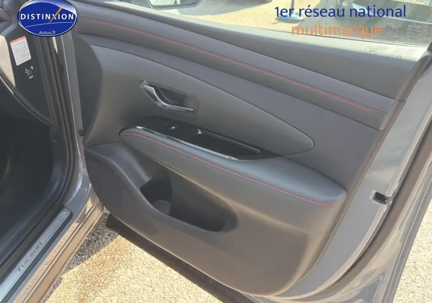 Vue intérieure de la porte avant gauche du Hyundai Tucson gris shadow avec surpiqûres rouges et poignée chromée.
