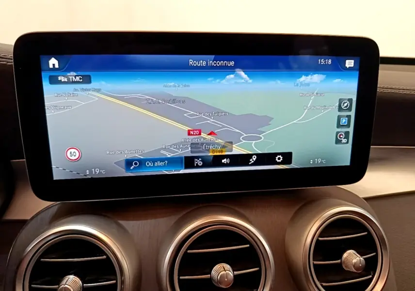 Écran tactile du système de navigation affichant une carte, avec trois aérateurs ronds en dessous, intérieur cuir marron.