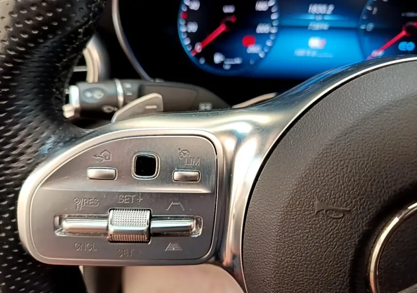 Gros plan sur les commandes du volant cuir et alu du Mercedes GLC 300 e AMG Line, affichage numérique en arrière-plan.